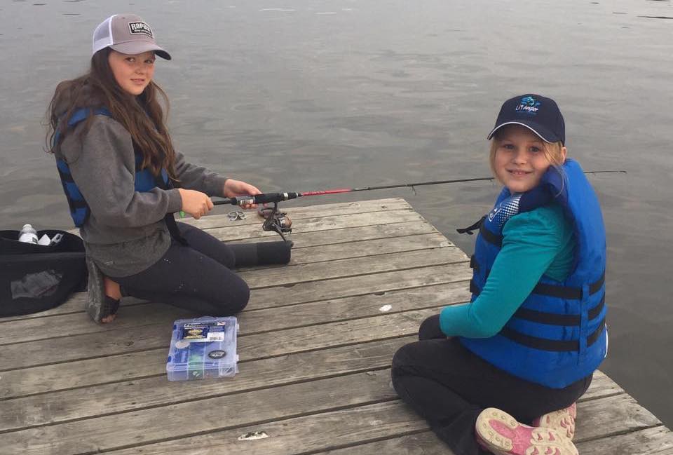 2 young girls sit on a dock fishing