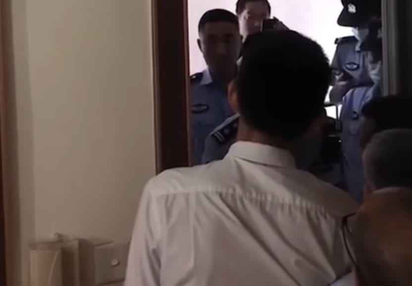 A man in white shirt stands on one side of a doorway while several officers dressed in blue uniforms stand on the other