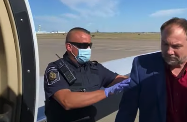 A video shot from the door of a small plan shows an officer standing with an arm on the pastor