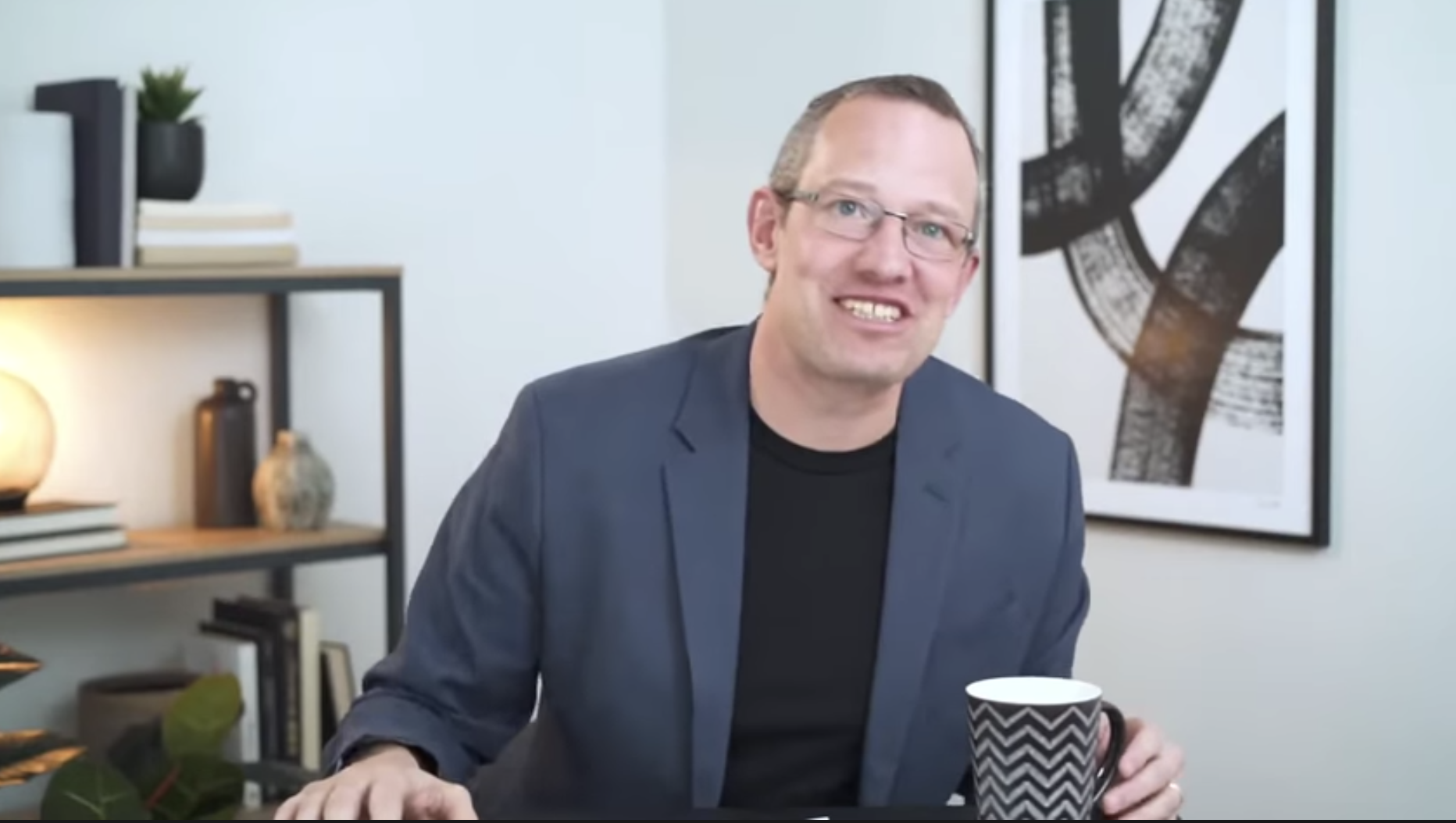 A man in a suit jacket and shirt sits at a table with a cup of coffee
