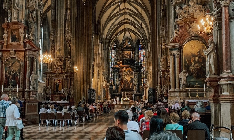 Inside St. Stephen's Cathedral in Vienna, Austria during peak tourist hour and mass service. Tall ceilings, stained glass, 