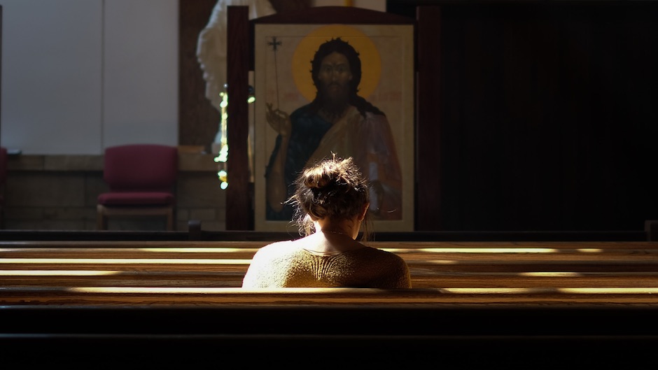 A woman sits in a pew praying. 