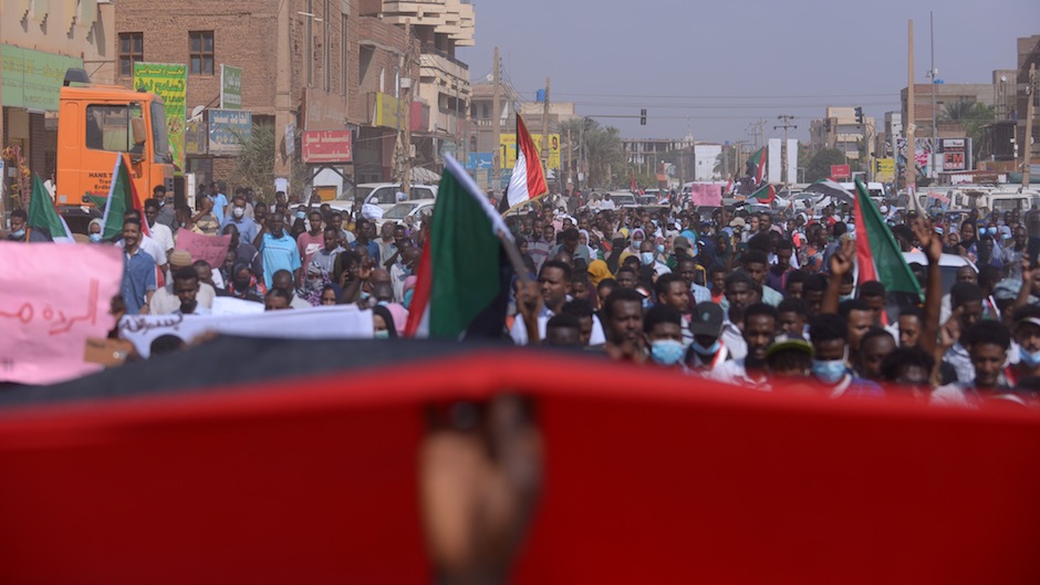 Crowds of people line the street with several Sudanese flags