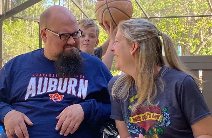 Jay Weaver sits and looks at his wife who is smiling at him while a son plays with a basketball behind them.