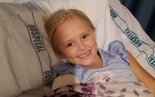 A young girl on a hospital bed smiles at the camera