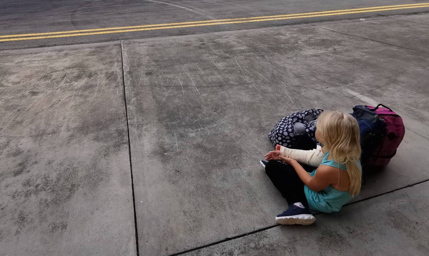 A young girl sits on the tarmac and waits