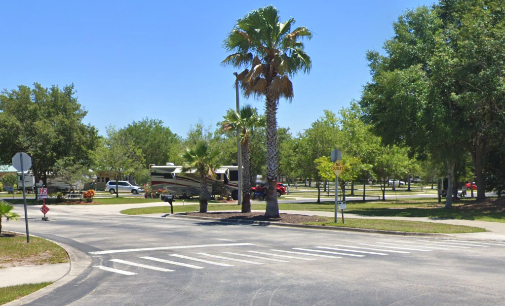 Palm trees stand at the entrance of the RV park with a motorhome in the background
