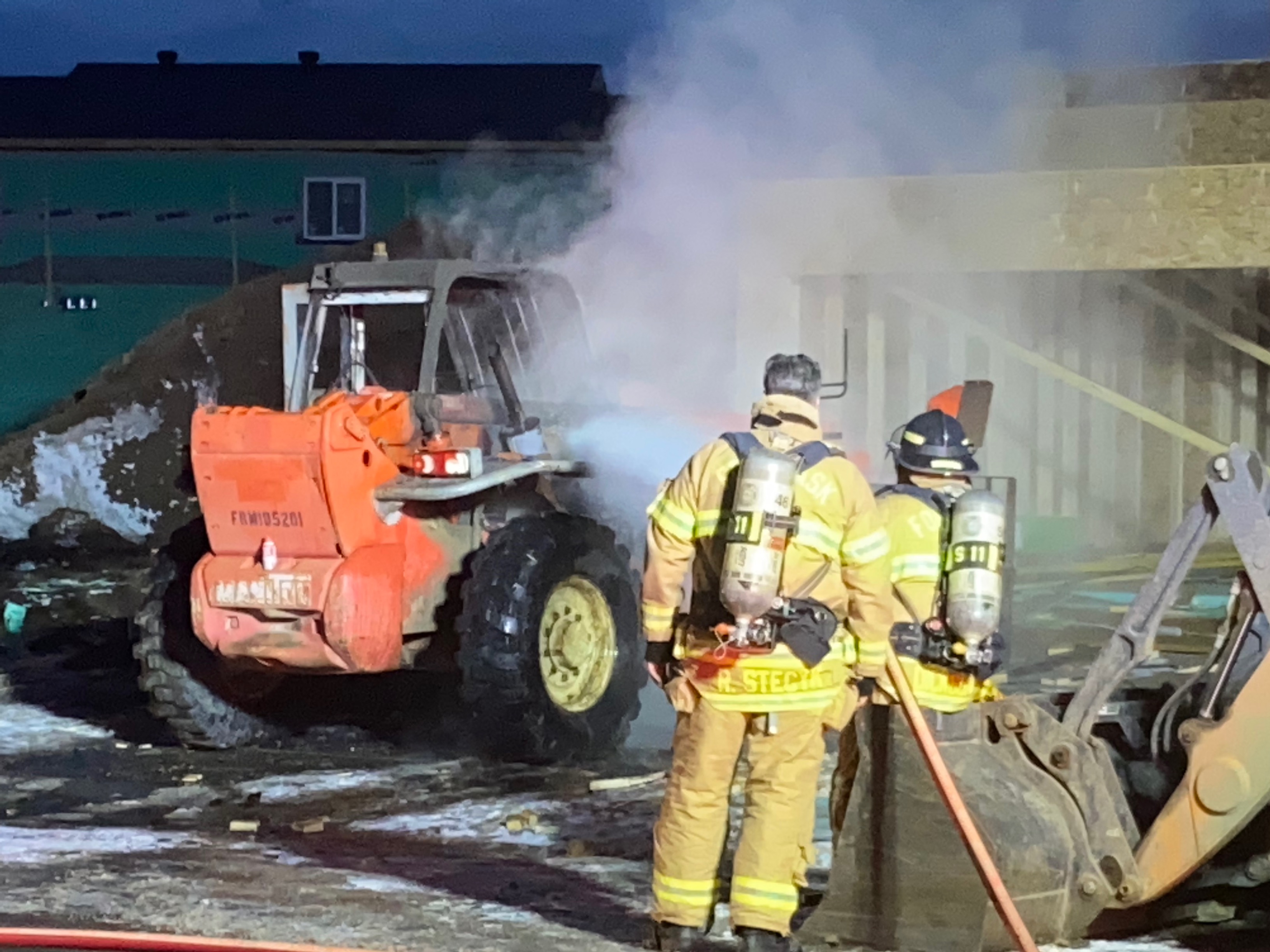 Firefighters in front of a smoking forklift.