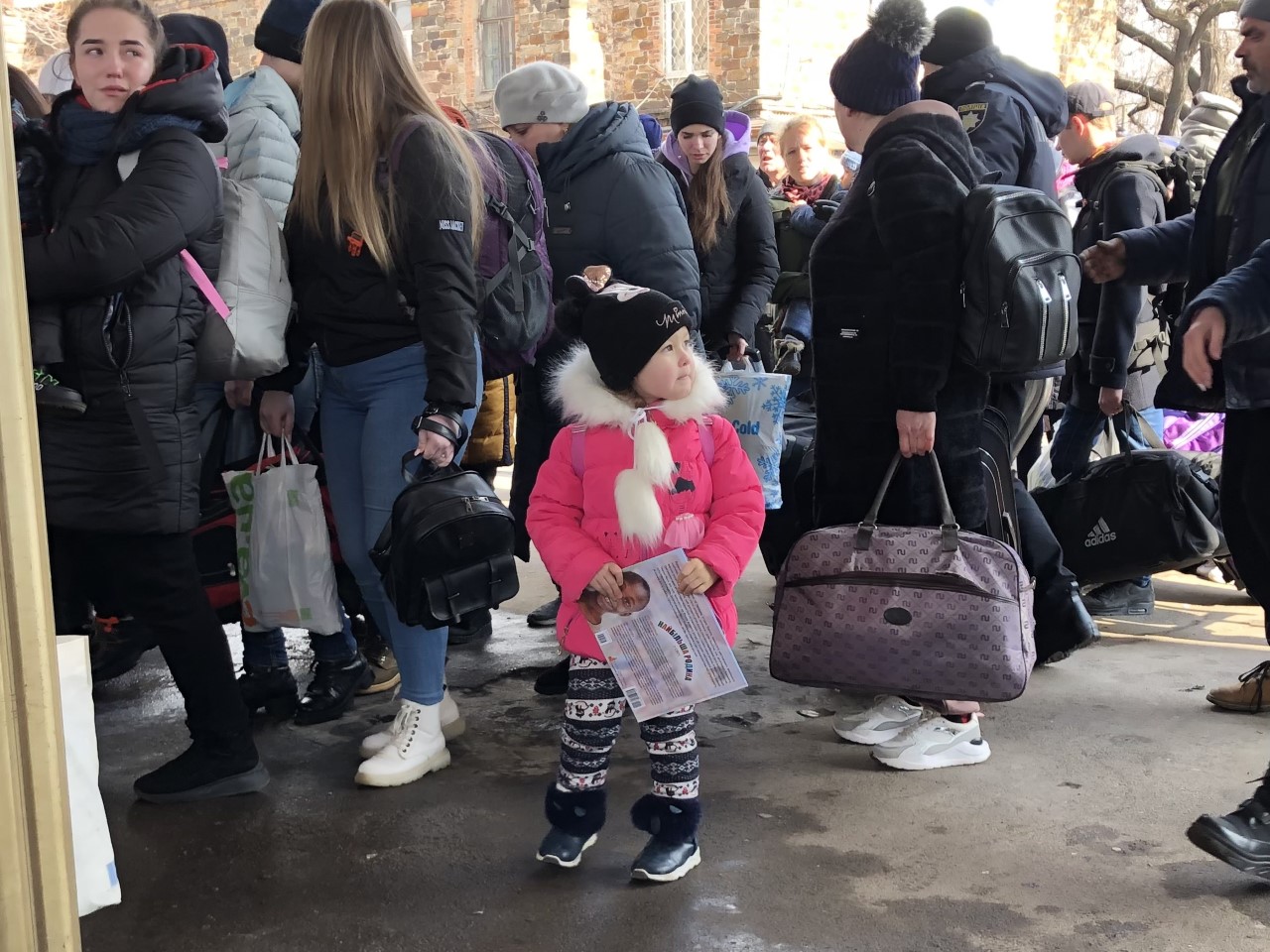 Little girl in a pink coat in the Ukraine, fleeing from the war, holding Paul Boge's book. 