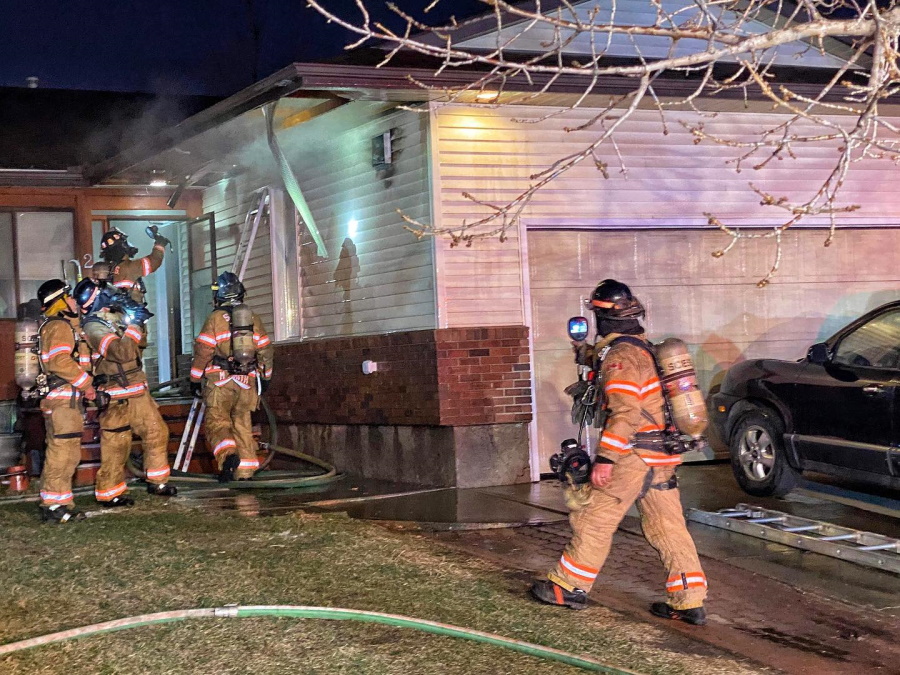 Firefighers looking at smoke coming out of an attic.