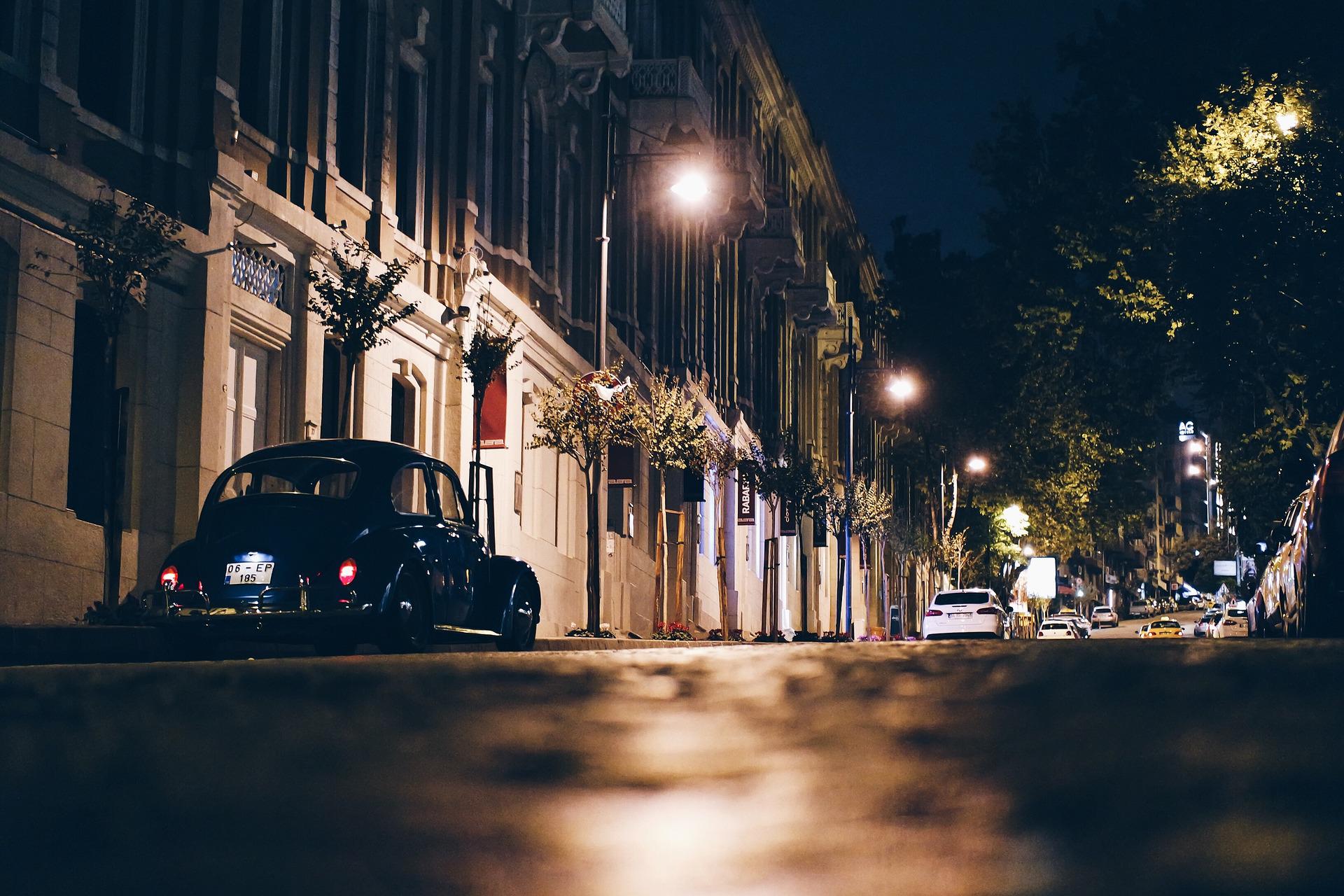 A street in a Turkish city at night time. An old VW Beetle is parked on the side 