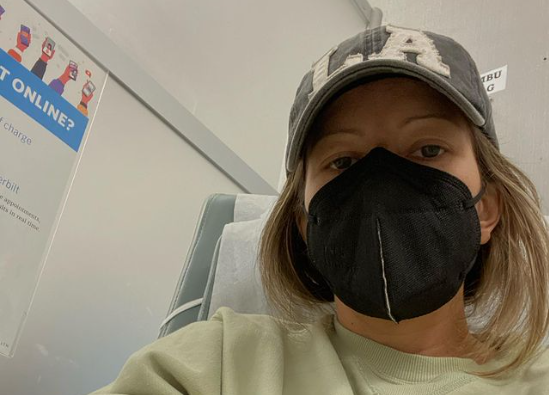 Selfie of Jodi King wearing a baseball cap and a mask in a hospital room