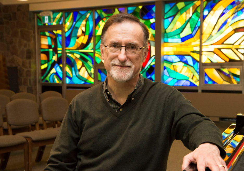 Ken Hull sitting on a piano bench with a stained glass window in the background
