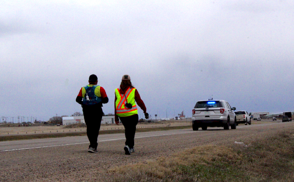 two individuals walking on the highway, escorted by RCMP.