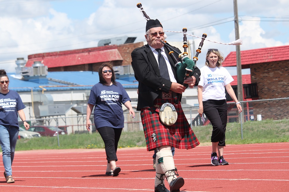 People walk behind man playing the bagpipes.
