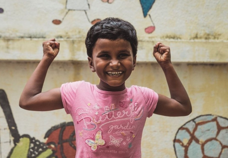 Dark-skinned little girl now free after being enslaved with her strong arms flexed. 