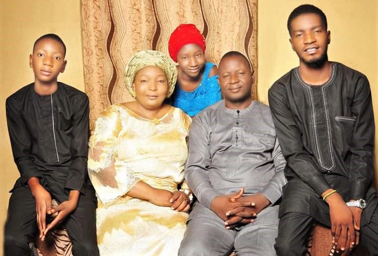 A mother and father sit in the centre of a family portrait with a boy on each end and a teen girl in  between mom and dad