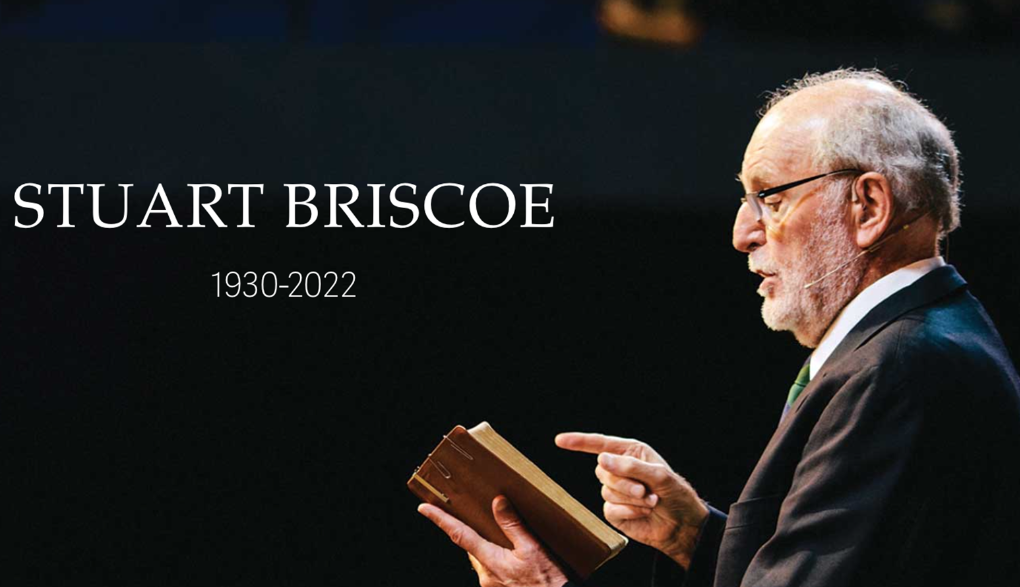 A side shot of a man with light skin tone and short balding grey hair. He speaks while holding a brown leather Bible. Text on the photo says "Stuart Briscoe 1930-2022"