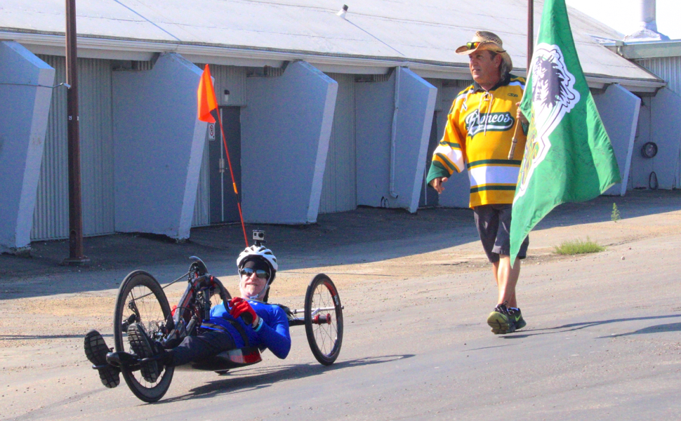 man walking beside a man on a hand cycle bike