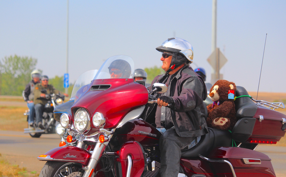 Man rides motorcycle with toys on the back.