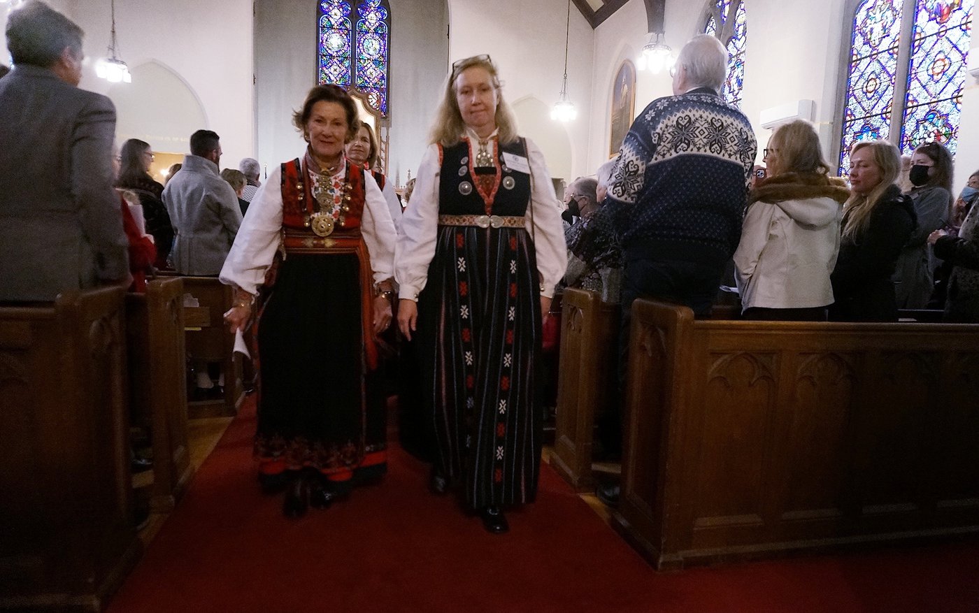 2 women dressed in long black dresses with colourful accents walk out of a church 