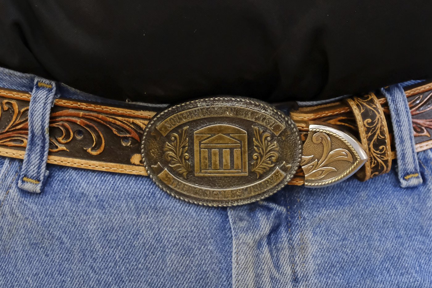 A bronze belt buckle is worn on a brown leather belt