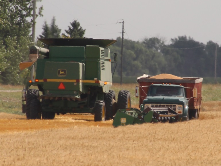 John Deere combine harvesting crop with a grain truck waiting in the field to load the grain