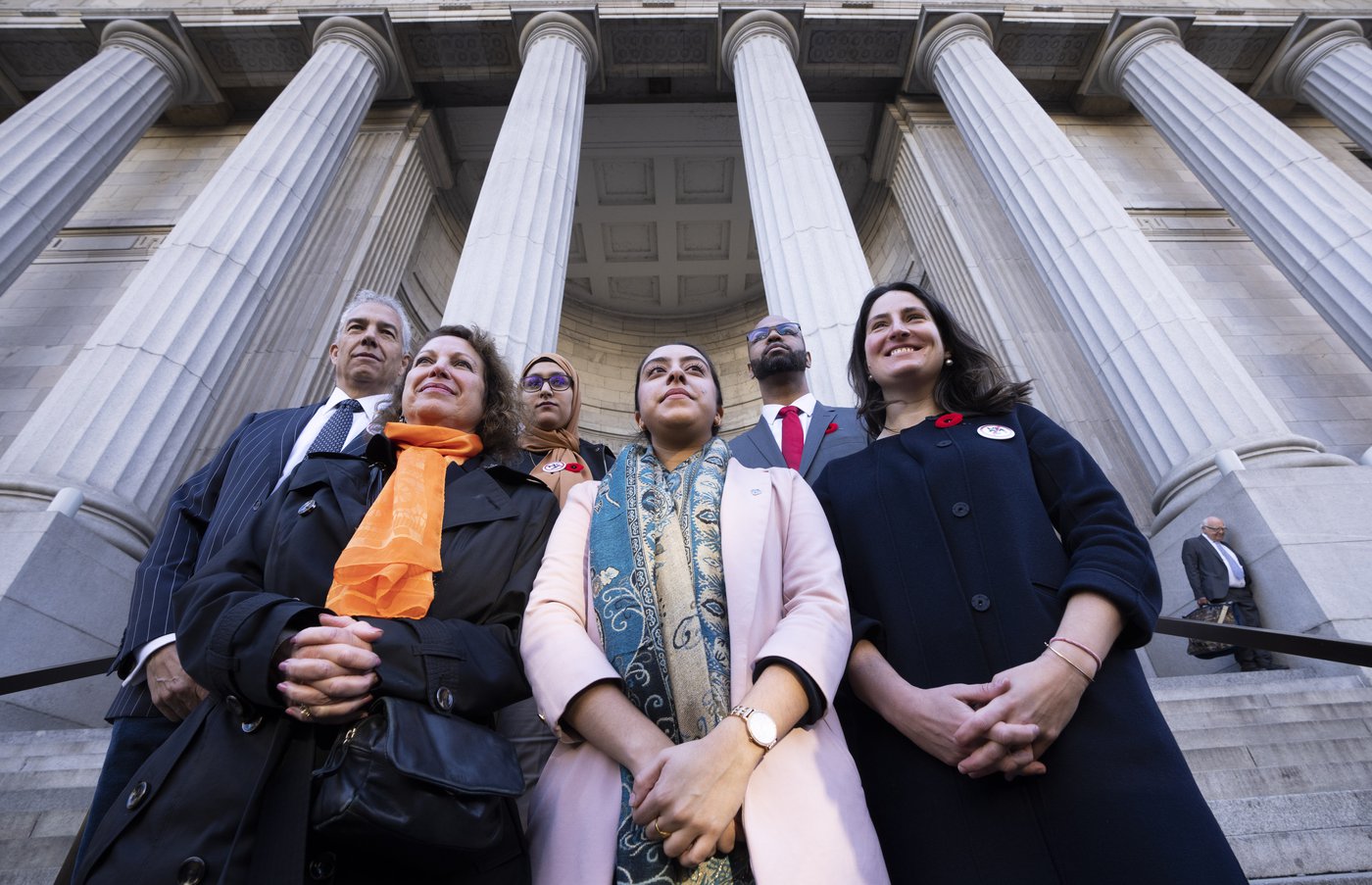 An upward angle shot of a group of six people. Taken from a very low angle, pillars from the front of a court building tower above them.