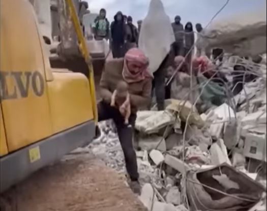 Screenshot from a video of a Syrian man carrying a newborn baby from the wreckage after a 7.8 magnitude earthquake hit the region.  