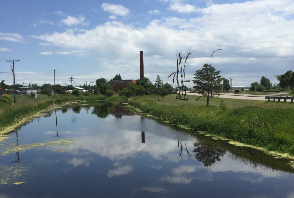 The Souris River in the foreground, with the reflection of the Soo Line Historical Museum on the water. 
