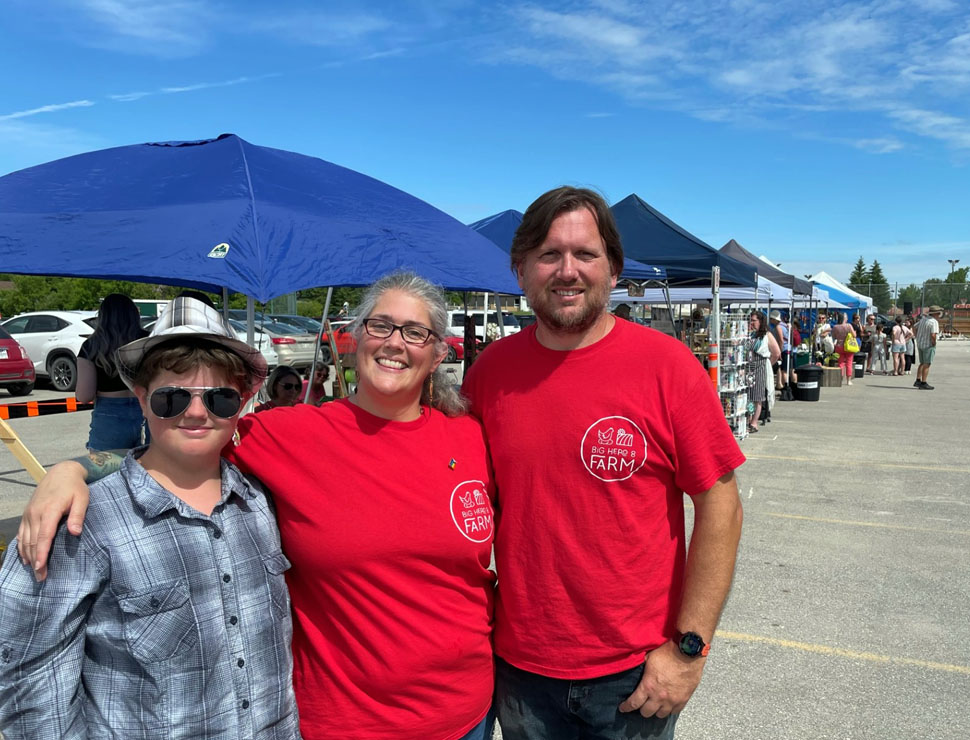 Faith, Sarah, and Vernon standing at the Farmers' Market in La Broquerie.