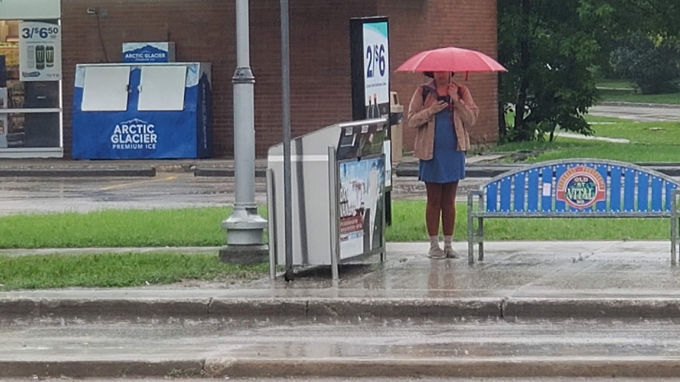 a woman stands under a red umbrella while it rains