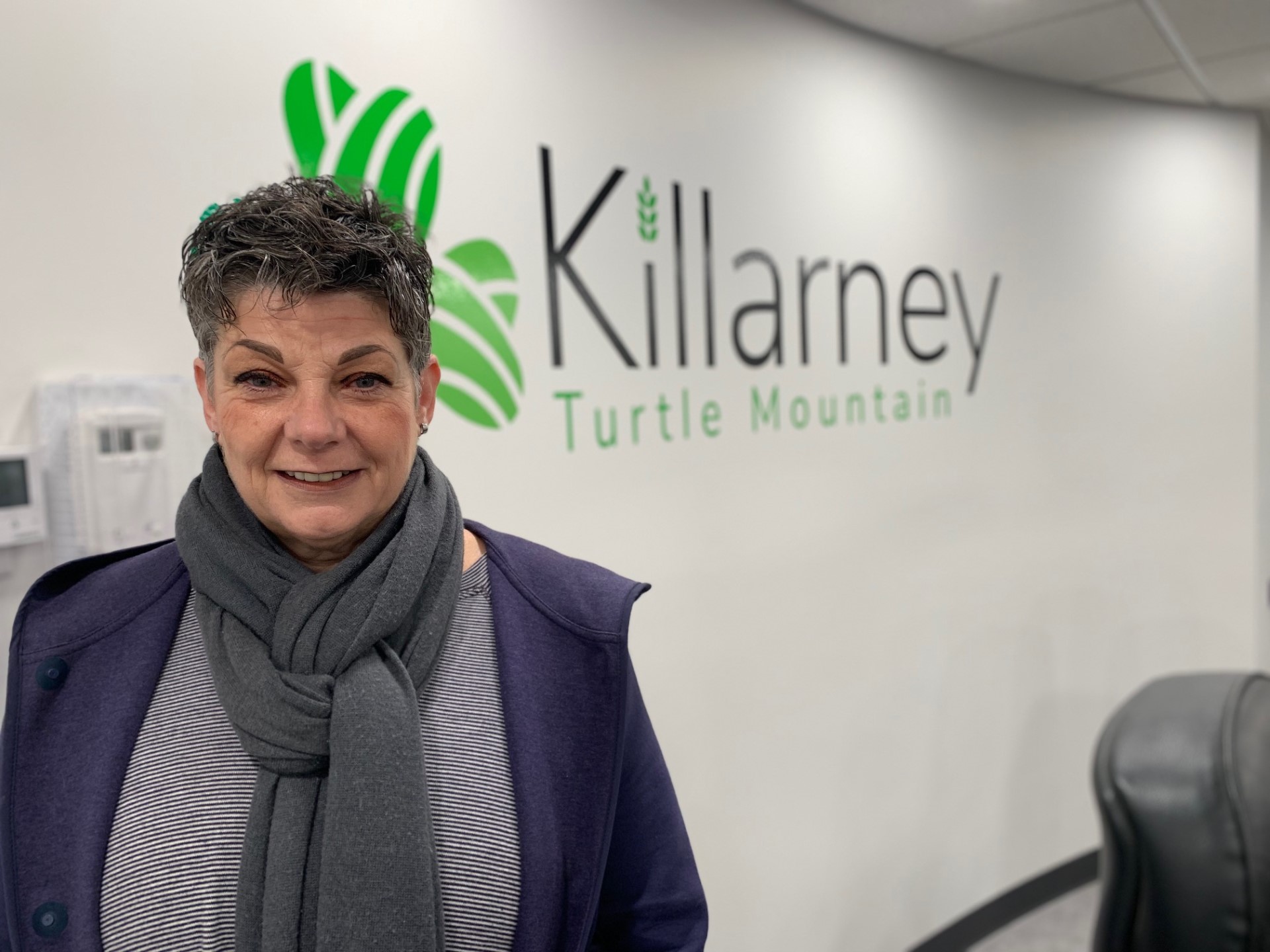 a lady wearing scarves in front of a sign that reads, 'Killarney Turtle Mountain'