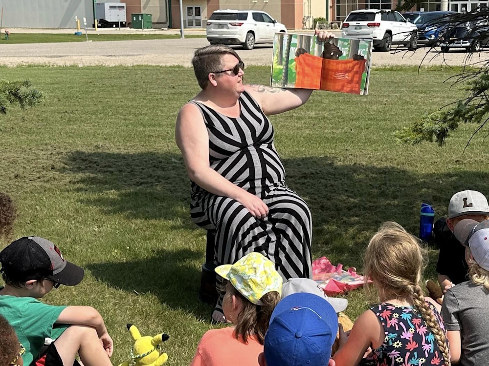 A young lady reading a story book to children outside in a park.