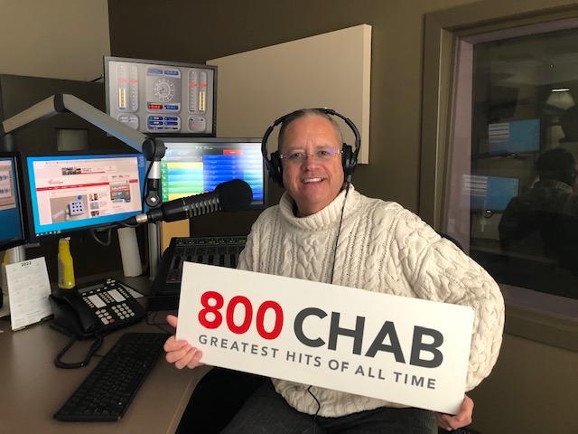 CHAB's Rob Carnie is shown here, in the CHAB studio, headphones on and holding a CHAB sign