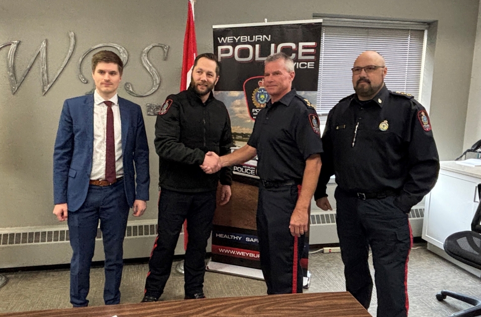 Four men standing in front of a Canadian flag and vertical banner that says police at the top