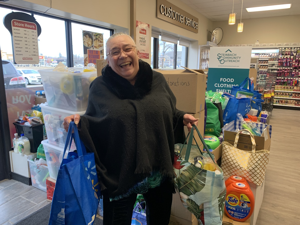 An amazing resident donating items to Soap for Hope in 2024. She is standing in Pharamasave, in front of a pile of donations!