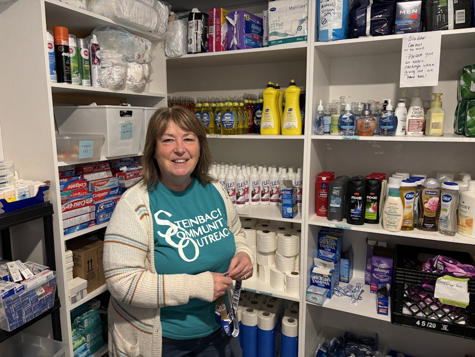 SCO's Executive Director stands in front of shelves full of soap thanks to the community for donating at Soap for Hope