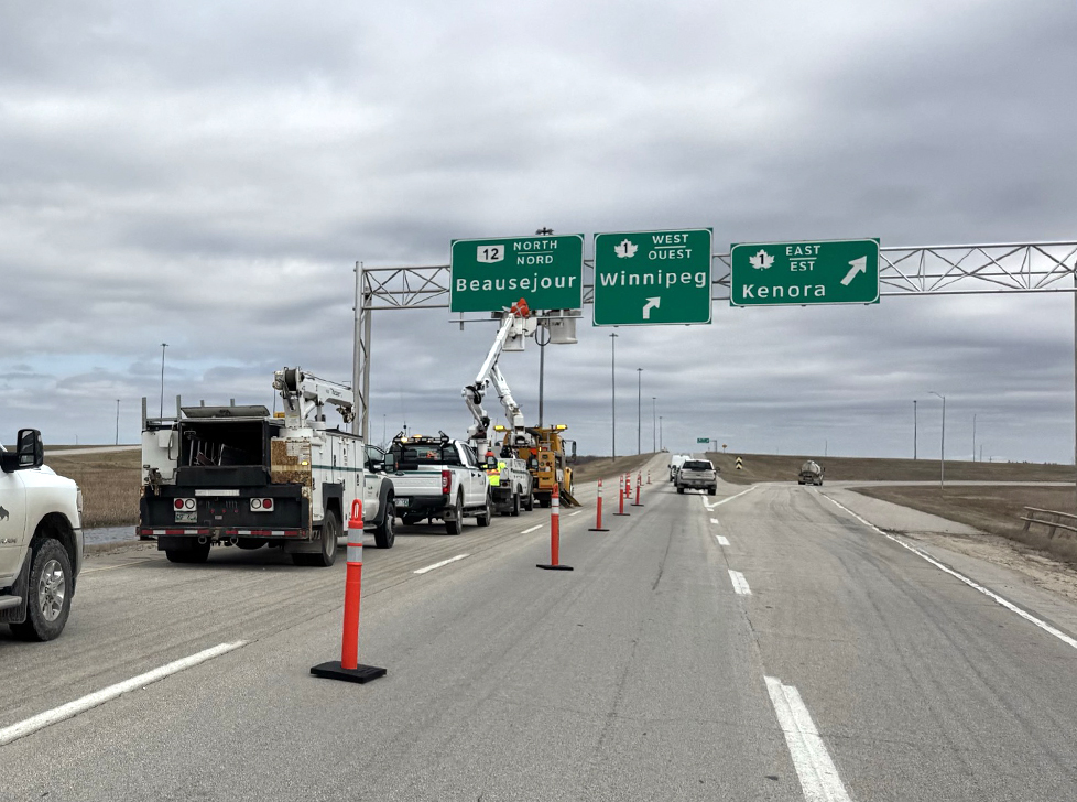 workers fix an overhead sign that reads Beausejour