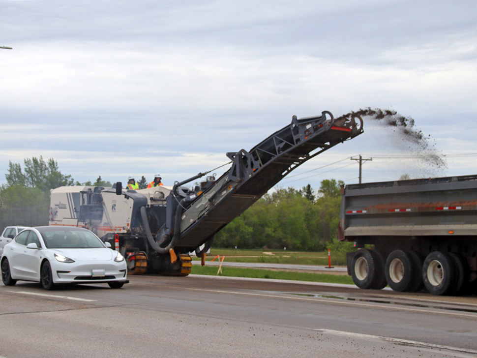 a pavement grinder dumping crushed up road into the back of a semi