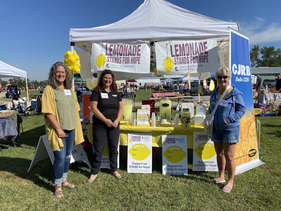 Three women standing near a lemonade stand with the CJRB banner behind