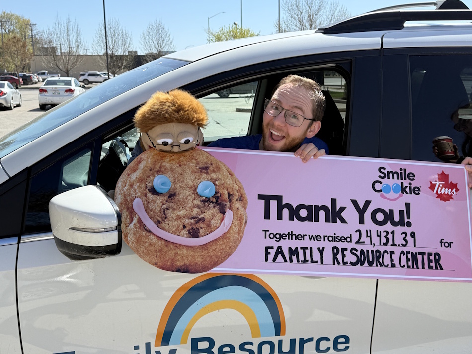 Puppet Peter trying to eat the smile cookie off the cheque from Smile Cookie Week with Peter Thiessen, Program Director at the FRC, holding the cheque