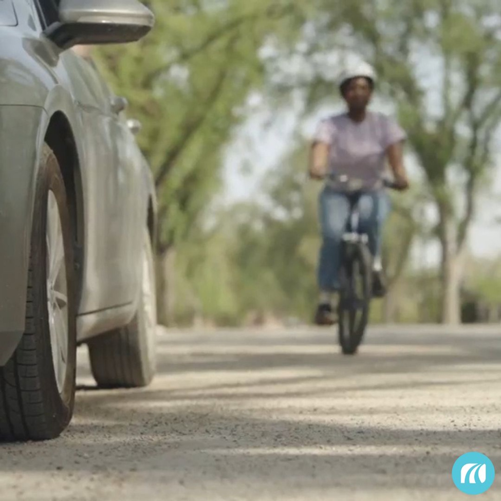 A GIRL RIDING A BIKE WITH A CAR DRIVING TOWARDS HER