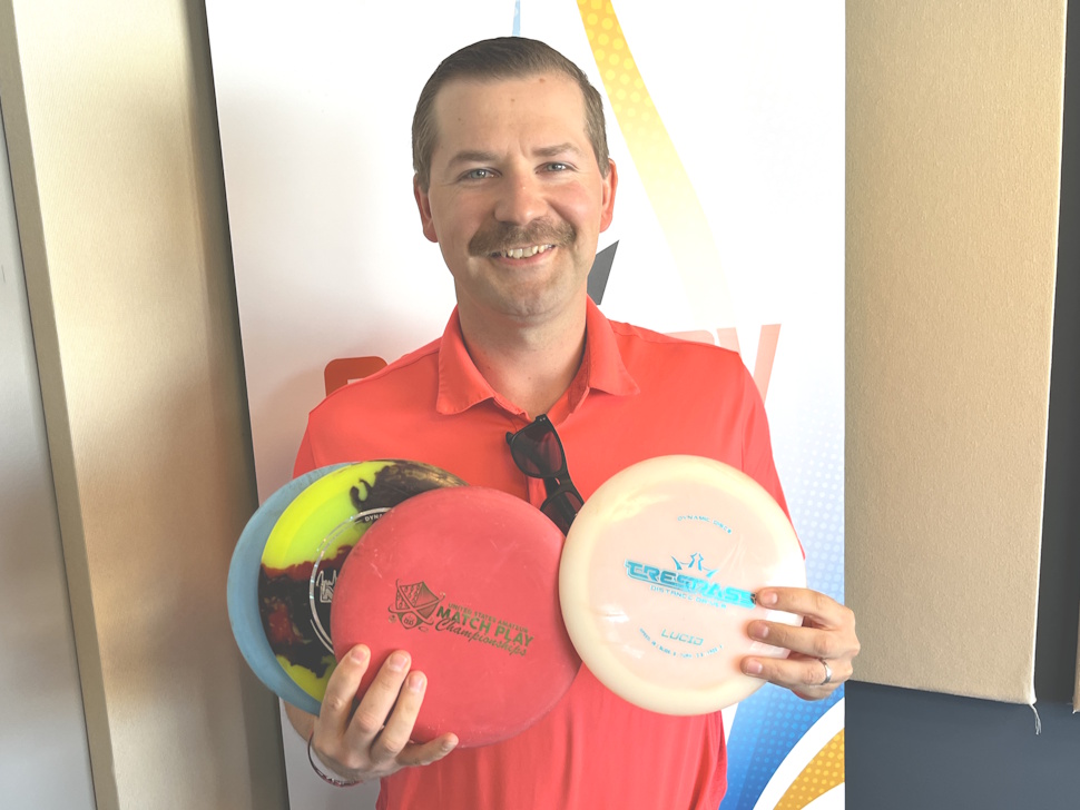Cody Buhler stands in the Country 93 radio studio holding several colourful disc golf discs.