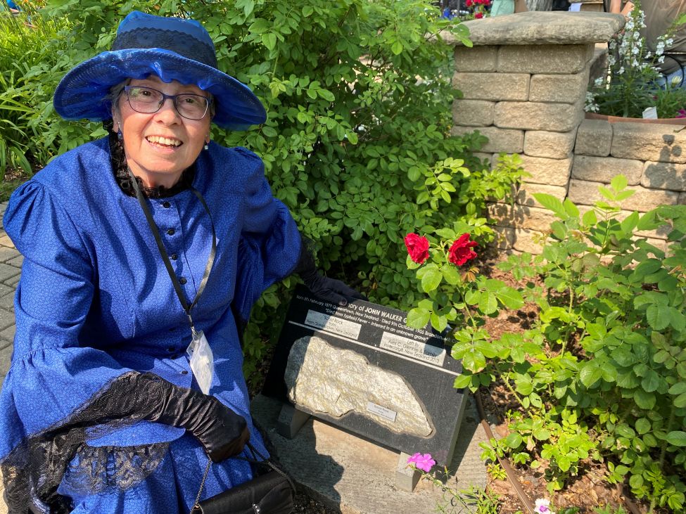 a lady kneeling beside a stone plaque and a rose bush