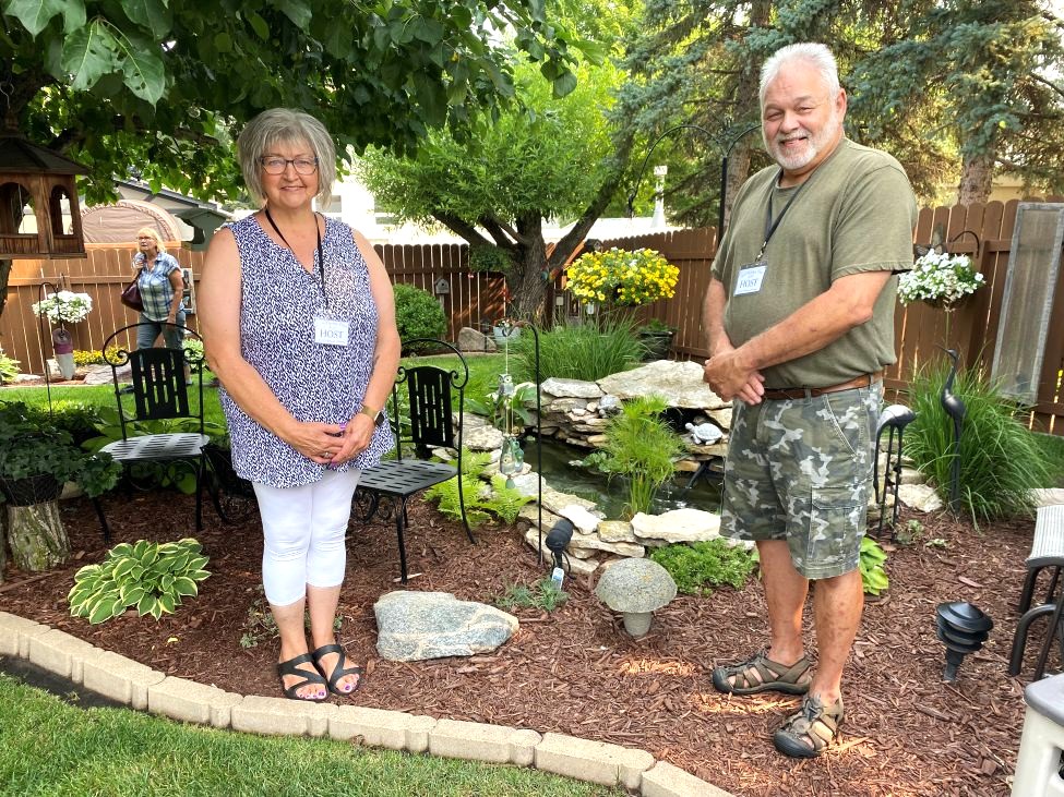 a man and a woman standing in their flower garden
