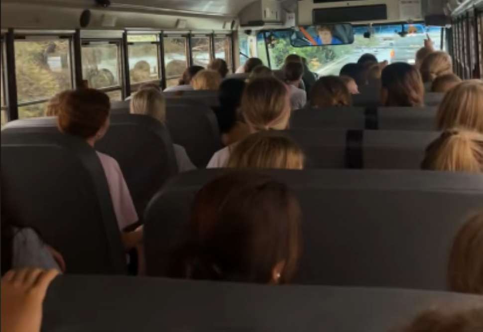 A screenshot from inside a bus shows the backs of young girls heads seated in rows
