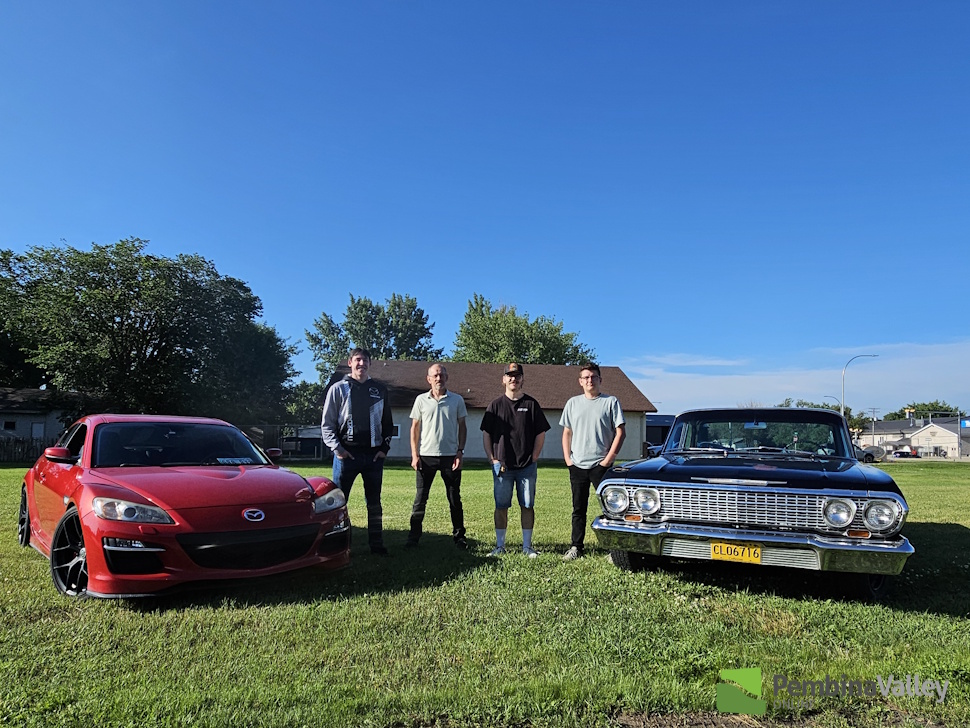 four men stand between two cars 
