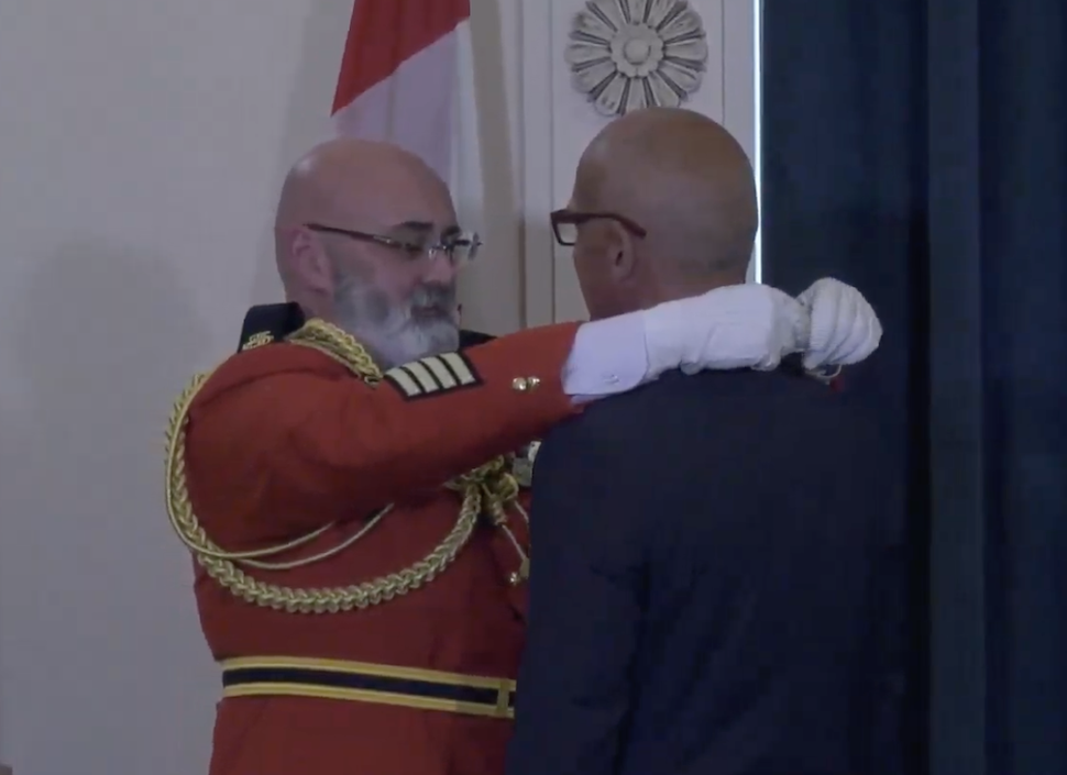 A Mountie in a dress uniform puts an award around the neck of a man