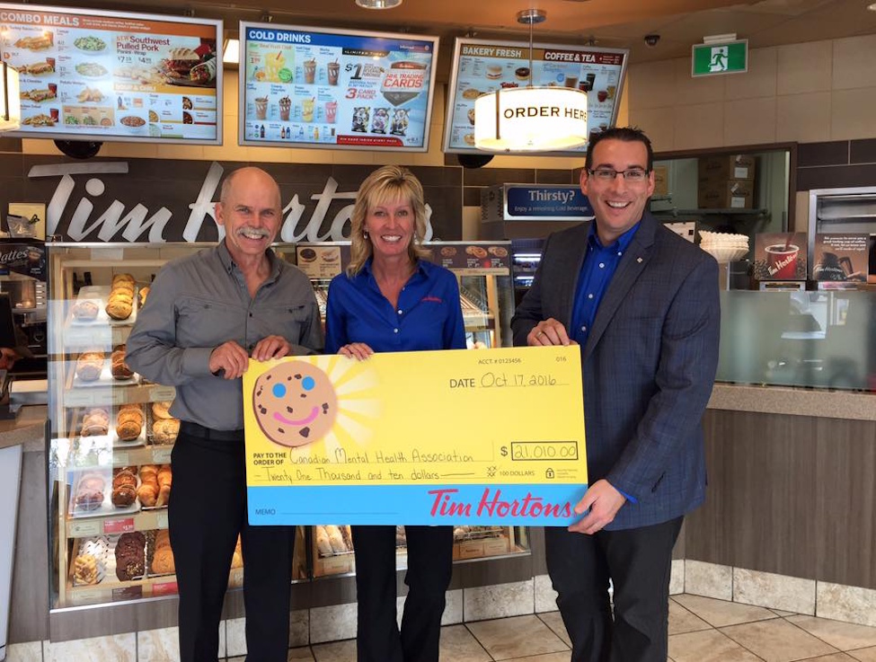 three people standing in a row with a giant cheque